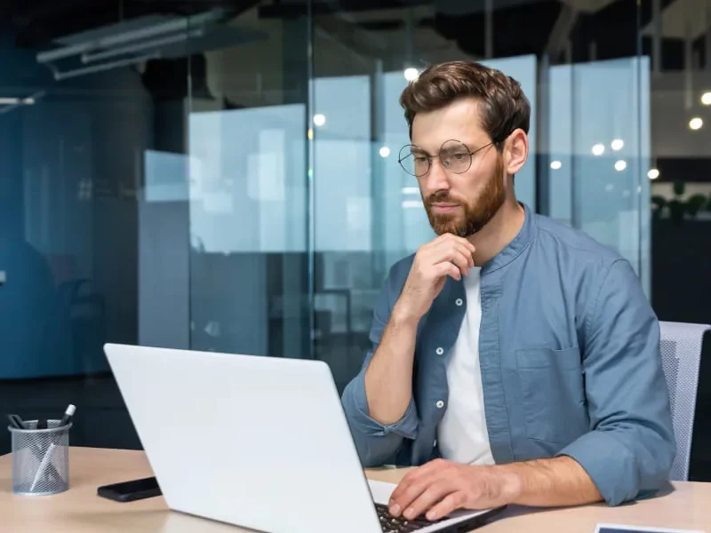 Un homme en lunettes assis à un bureau avec un ordinateur portable